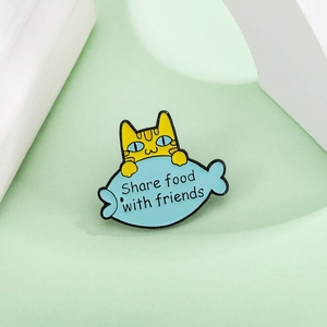 Detail view of cartoon enamel pin showing a yellow cat with a blue fish and text