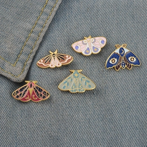 Set of 5 celestial moth enamel pins with moon and star patterns on denim backdrop