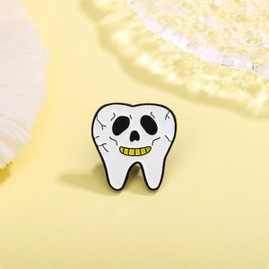 Detail shot of a white tooth enamel pin with a skull face and gold teeth design