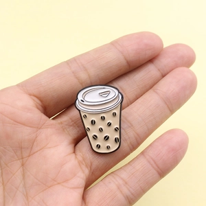 Cute coffee cup enamel pin brooch featuring black bean patterns held in hand for scale