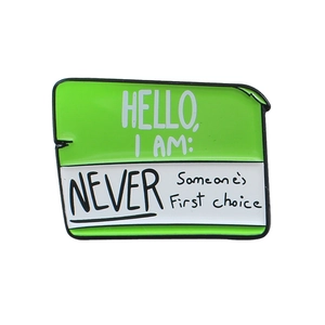 Creative enamel pin badge featuring a green name tag with 'Never Someone's First Choice' text