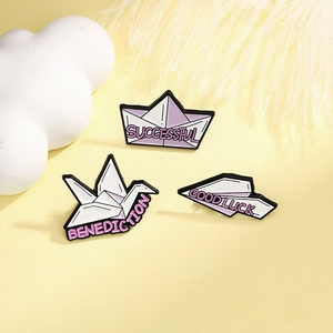 Minimalist origami enamel pin set with paper crane and airplane on soft yellow background