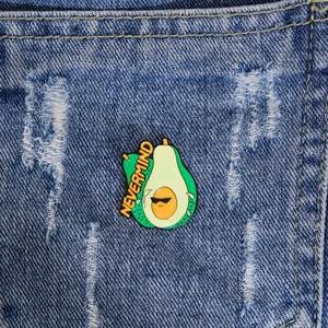 Cute avocado enamel pin with sunglasses and Nevermind text on blue denim fabric