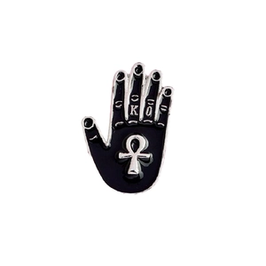 Detail showing hand-shaped black enamel pin with silver Ankh symbol and gothic lettering