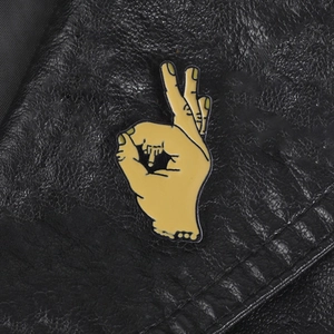 Edgy yellow enamel OK sign hand gesture brooch pin on black leather surface