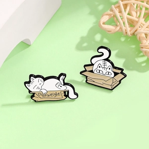 Detail of two funny enamel cat pins featuring a white cat on an overweight box and a hiding cat