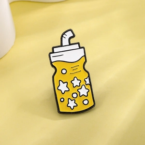 Cute yellow enamel bottle pin with white stars and straw on soft yellow background