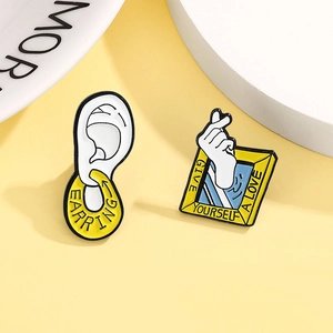 Close-up of creative enamel pins featuring ear with earring and heart gesture frames