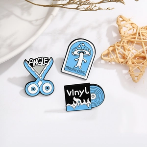 Dettaglio di spillette in smalto blu con forbici a occhio, fungo e disco in vinile