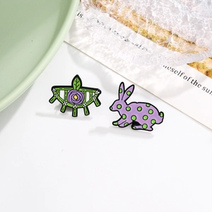 Cartoon rabbit and purple rose enamel pin set with leaf and fence motifs on a white surface