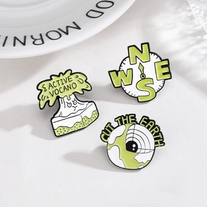 Three enamel pins featuring active volcano, compass and earth designs on white plate
