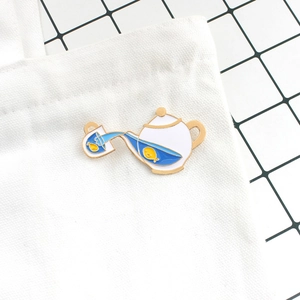 Detail of creative enamel teapot brooch with small fish pinned on white canvas bag