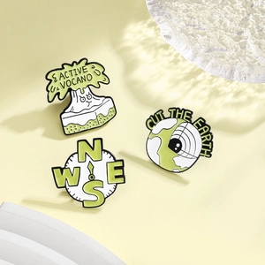 Three-piece set of cartoon enamel pins featuring volcano, earth, and compass motifs