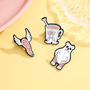 Close-up of surreal enamel pins featuring a winged ear and quirky creature designs