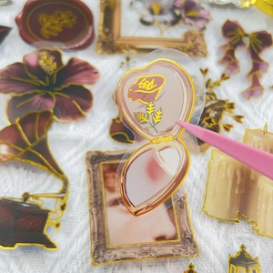 Macro detail of vintage PET sticker with gold foil edge using tweezers for craft decoration