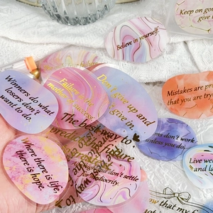 Detail of macaron pastel stickers with gold lettering on white textured fabric background
