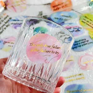 Detail of waterproof PET stickers with gold foil text on a textured glass cup