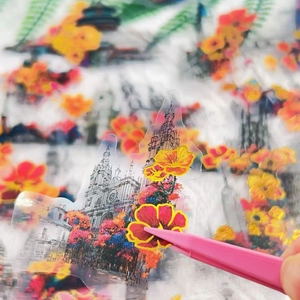Close-up of hand using pink tweezers to apply transparent floral and building stickers