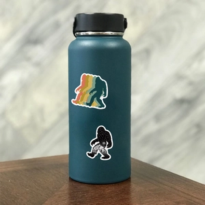 Close-up of decorative Bigfoot silhouette stickers on a matte dark teal vacuum flask