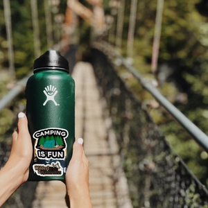 Waterproof camping stickers on a green sports water bottle with a scenic forest background