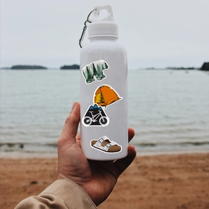 Outdoor sport water bottle with mountain bike and camping stickers on beach background
