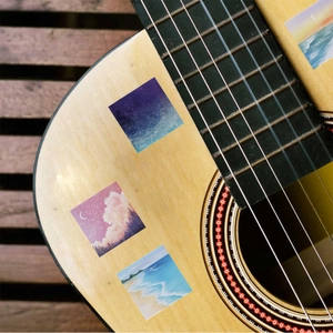 Artistic landscape stickers applied on a wooden guitar featuring scenic oil painting patterns