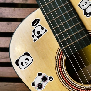 Close-up of waterproof cartoon panda stickers on a light wooden acoustic guitar surface