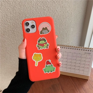 Detail of red silicone phone case with cute cartoon frog stickers held against a wall