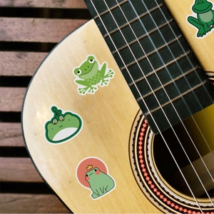 Detailed view of cute green frog cartoon stickers applied on a smooth guitar surface