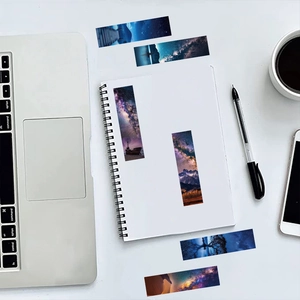 Scattered galaxy bookmarks on a white desk next to a notebook and coffee cup