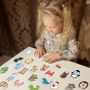 Toddler playing with colorful waterproof cartoon animal stickers on a white desk
