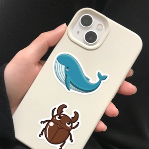 Detail of hand holding beige matte iPhone case with cartoon whale and beetle stickers