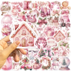 Gros plan d'une main tenant un autocollant de Noël rose avec motif de maison en pain d'épice