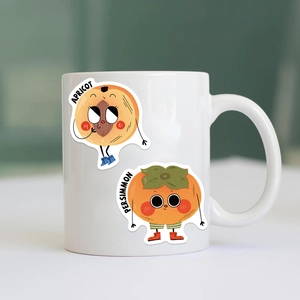 Close-up of white ceramic mug with cute cartoon apricot and persimmon fruit illustrations