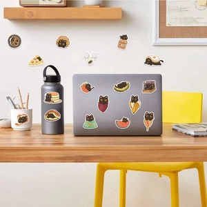 Dettaglio di adesivi doodle di gatto nero applicati su laptop e borraccia in acciaio