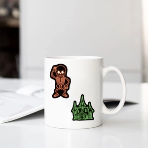 Close-up of Halloween neon stickers with skull and castle on a white ceramic mug