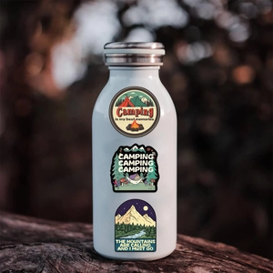 Detail view of waterproof camping stickers on a white metal bottle with forest background