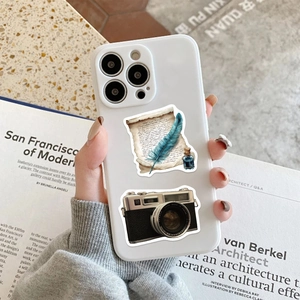 Detalle de pegatinas retro de cámara y pluma en una funda de teléfono blanca