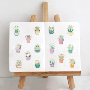 Detailed view of cute cartoon cat cactus stickers on a white grid notebook page