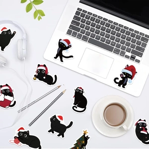 Christmas black cat stickers shown as lifestyle decor on a laptop and desk setup