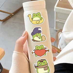 Detail of four cute cartoon frog stickers applied on a cream-colored insulated tumbler mug