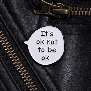 Macro detail of 'It's ok not to be ok' enamel pin on black leather material background