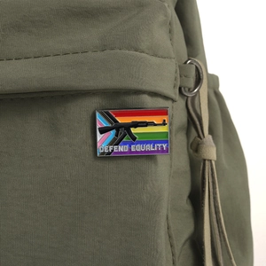 Detail of Defend Equality rainbow enamel pin with rifle silhouette on green fabric