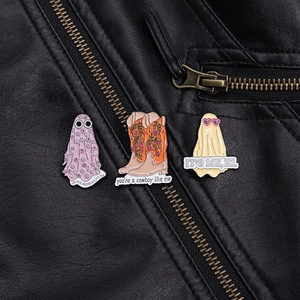 Three enamel pins including ghosts and floral boot on a black leather jacket lapel
