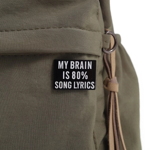 Close-up of black rectangular enamel pin with white text on olive canvas fabric