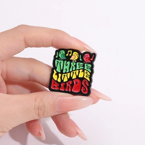 Three Little Birds bunter Emaille-Anstecknadel-Badge mit Reggae-Farben in der Hand