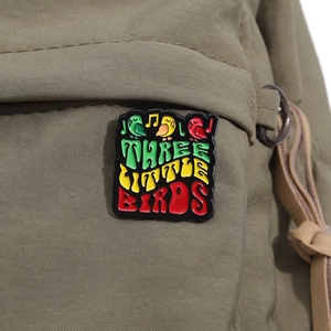 Nahaufnahme der Three Little Birds Emaille-Anstecknadel mit Noten auf einer Segeltuchtasche