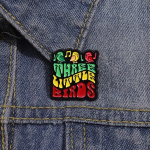 Detailansicht der Three Little Birds Emaille-Anstecknadel auf Denim mit bunten Vögeln