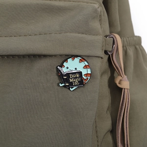 Detailed view of an enamel cookie pin reading Dark Magic 101 on a green canvas backpack