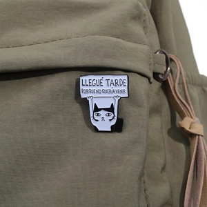 Detailed close-up of funny cat enamel pin with Spanish text on dark green canvas fabric